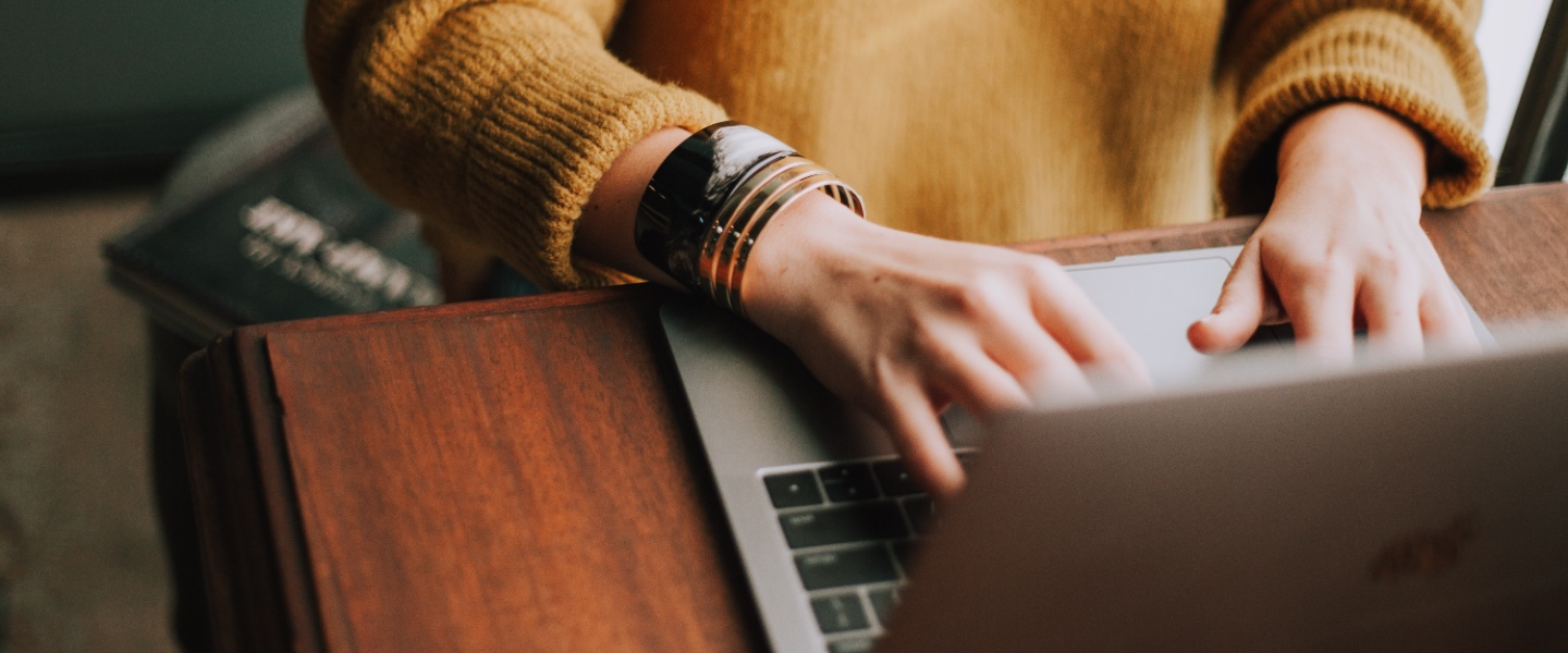 carnê-leão: mãos femininas usando um notebook com suéter mostarda em uma mesa de madeira