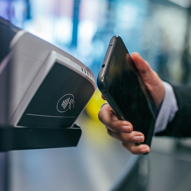 Carteira digital: fotografia de uma mão aproximando um celular de uma máquina com o símbolo de pagamento por aproximação