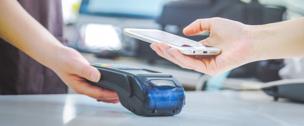 NFC: imagem de uma mão segurando a maquininha de cartão e outra com celular aproximando para pagamento