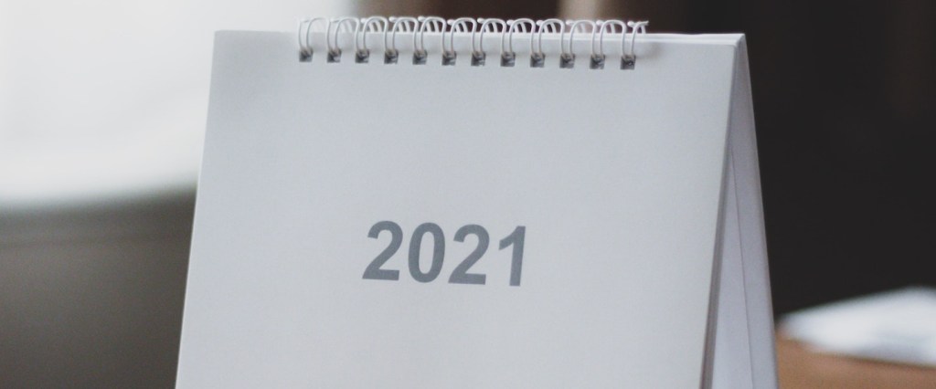 Calendário Auxílio Emergencial 2021 Bolsa Família: fotografia de um calendário de mesa branco, com o número 2021 em cinza no meio, sobre uma mesa de madeira