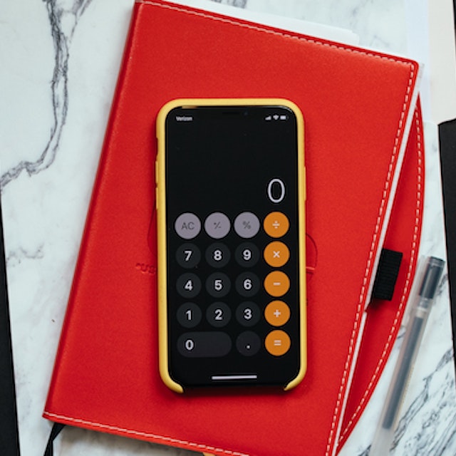 imagem de um celular aberto na calculadora em cima de um bloco de notas vermelho