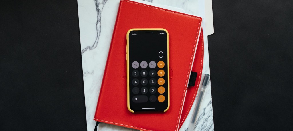 imagem de um celular aberto na calculadora em cima de um bloco de notas vermelho