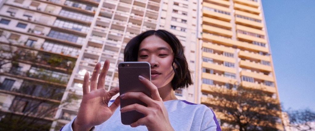 pagamentos com o pix: mulher segurando um celular em frente a um prédio