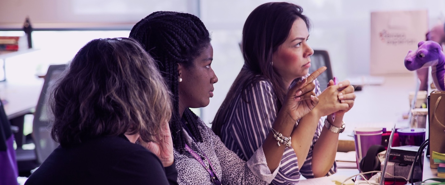 APM PROGRAM: Foto mostra três mulheres sentadas em frente a uma tela de computador, no escritório do Nubank