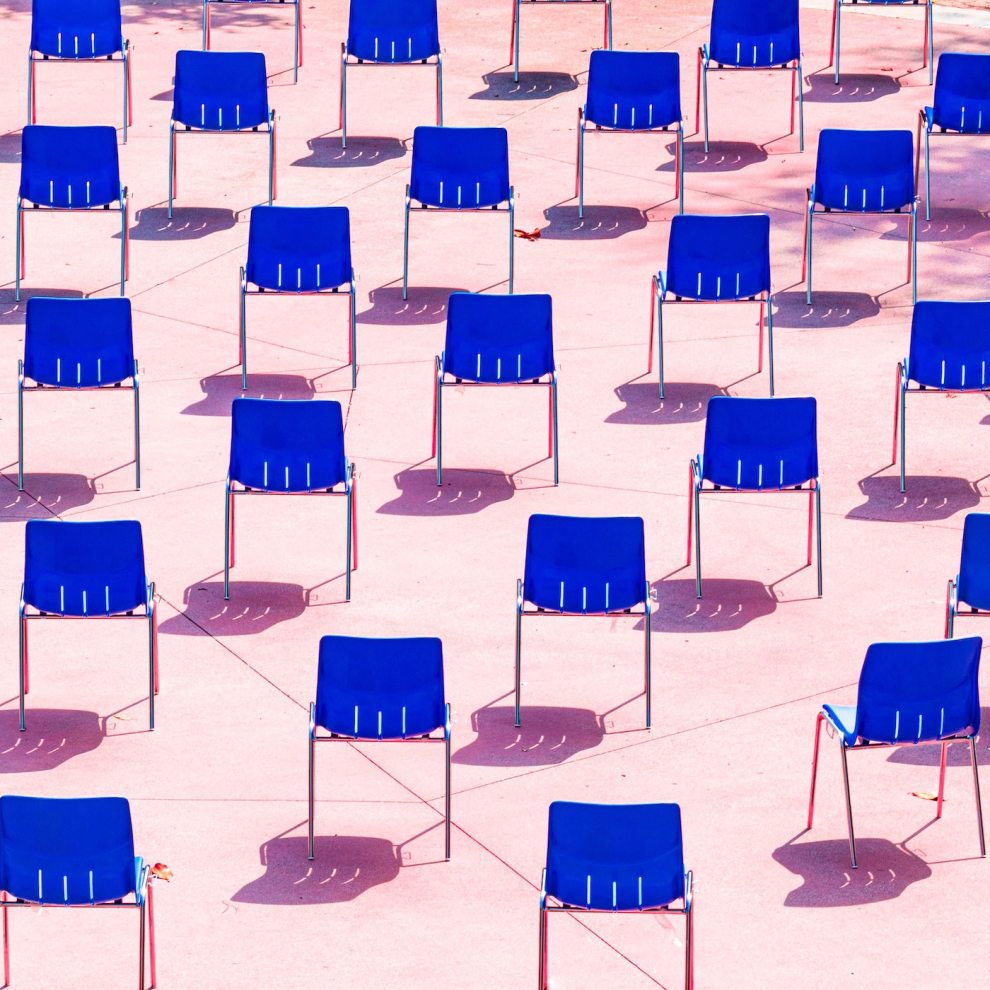 Dezenas de cadeiras azuis de costas dispostas em um fundo rosa claro