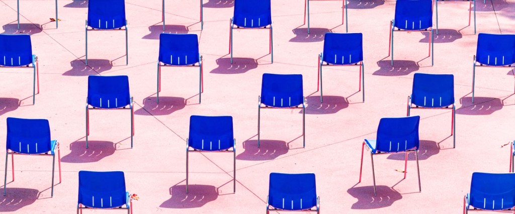 Dezenas de cadeiras azuis de costas dispostas em um fundo rosa claro