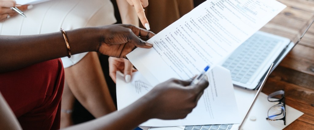 momento certo investimentos empresa: mulher negra empreendedora segurando um papel, caneta e apresentando o documento para outras pessoas