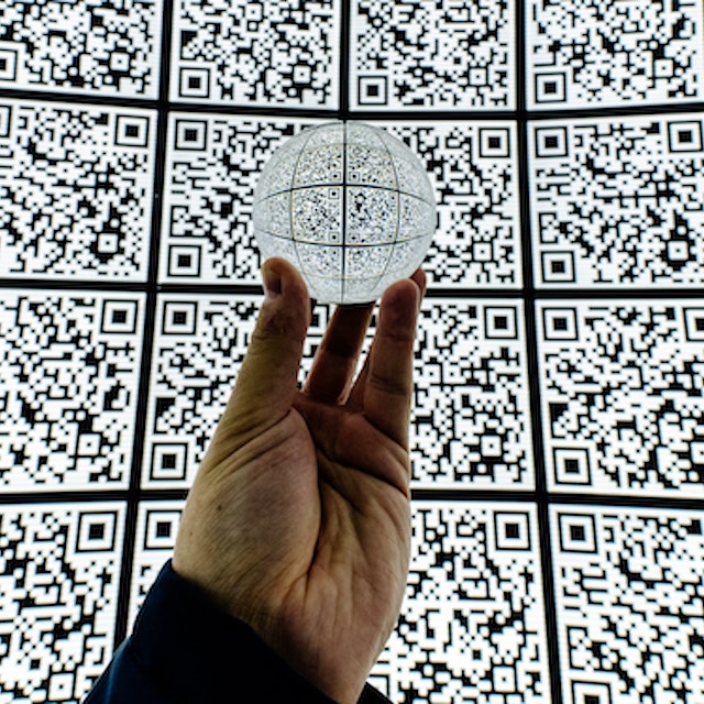 uma mão segurando um globo de QR Code em frente a um mural de QR Code