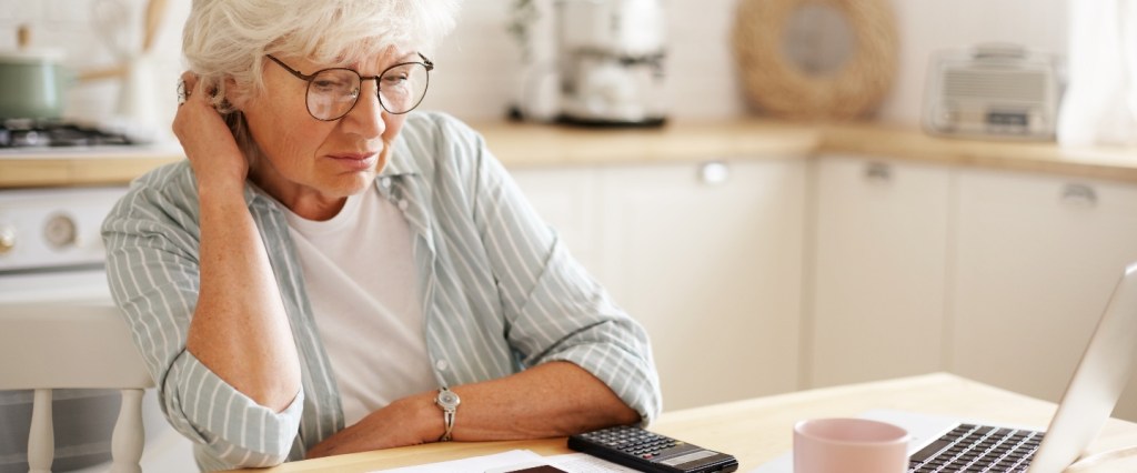 parar de contribuir inss: senhora idosa em frente ao computador fazendo cálculos com feição preocupada