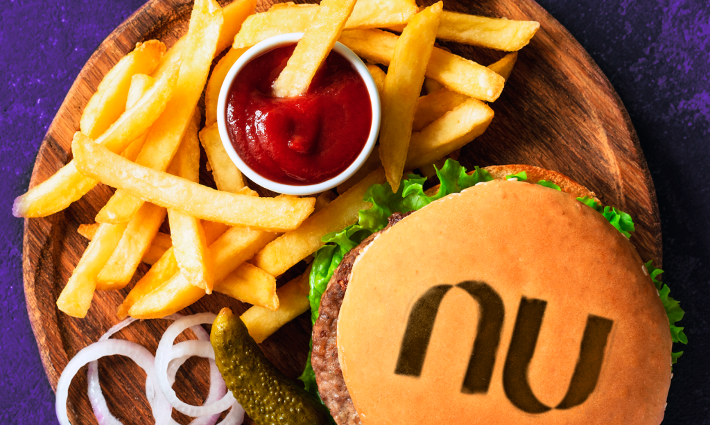 hambúrguer com o logo do Nu e batatas fritas com catchup e cebola em uma bandeja com um fundo roxo