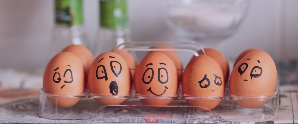Foto de ovos em uma caixa transparente com rostos desenhados em canetinha . Crédito: Photo by Tengyart on Unsplash