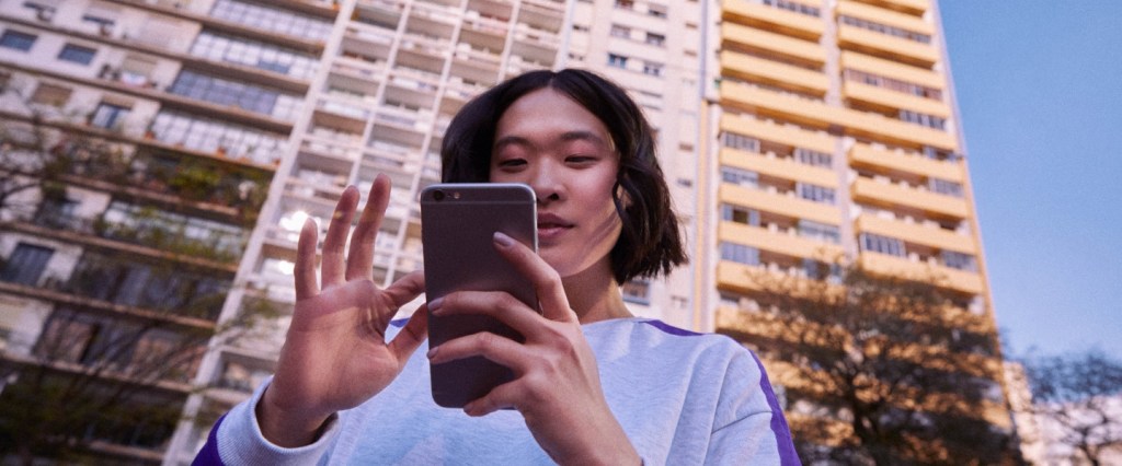 Nubank não tema agência física: mulher asuática olha o celular com um prédio ao fundo