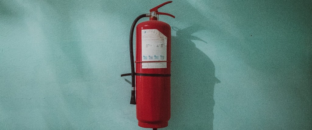 auxílio emergencial: extintor de incêndio vermelho com uma parede verde de fundo. Foto: Piotr Chrobot @Unsplash