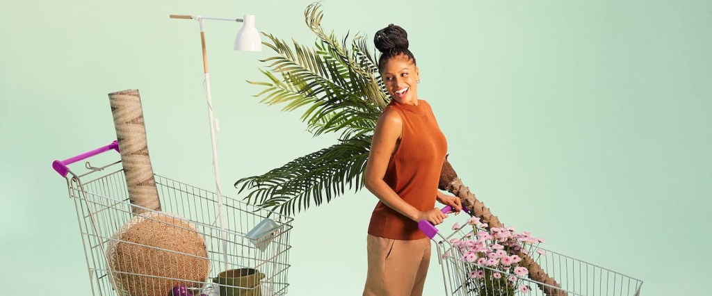 Como proteger o cartão de crédito: imagem de uma mulher negra empurrando um carrinho de compras num cenário de fundo verde. Ao lado dela, há um outro carrinho. Ambos estão com objetos dentro dele. A mulher usa uma roupa marrom e o cabelo está preso em um coque bem alto.