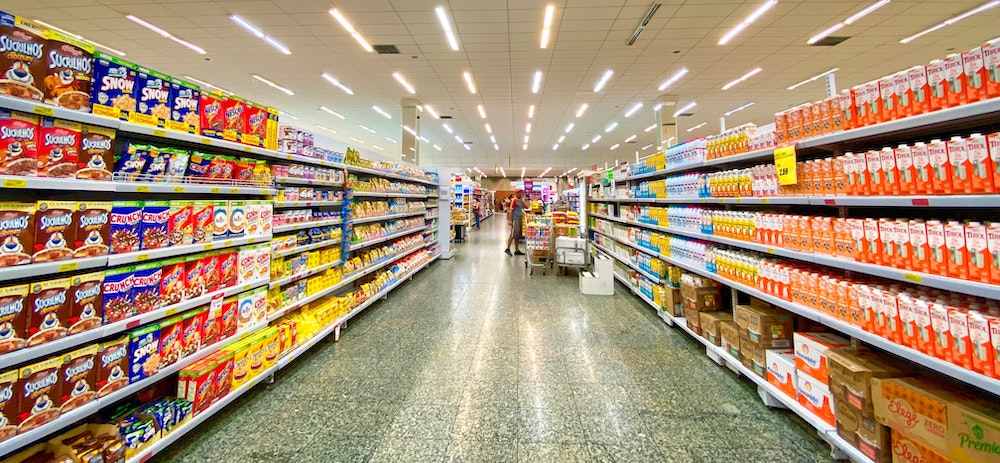 Foto de um corredor de supermercado com cereais de um lado e leite do outro.