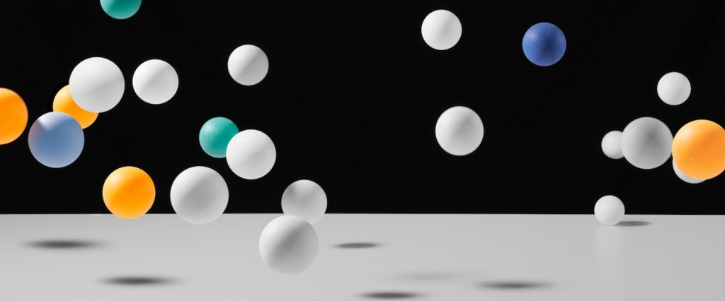 Calendário terceira parcela Auxílio Emergencial 2021: fotografia mostra bolinhas de ping pong brancas, verdes, azuis e laranjas caindo sobre uma superfície branca. Créditos: Ellen Qin
