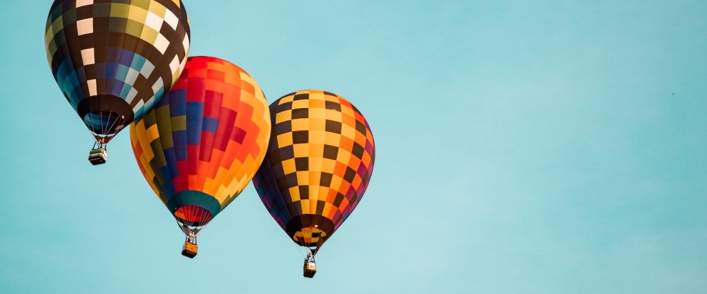Terceira parcela auxílio emergencial: fotografia de três balões voando com o céu azul ao fundo. Créditos da imagem: Aaron Burden