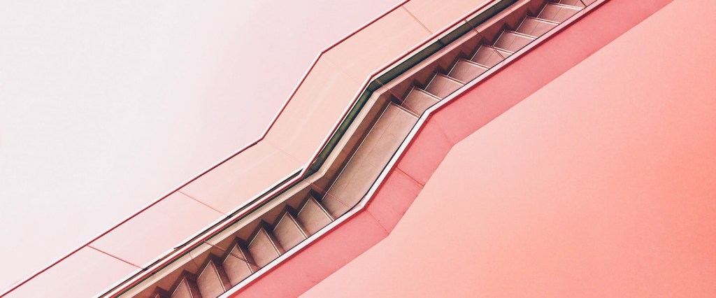 escada rolante subindo em frente a um fundo rosa claro