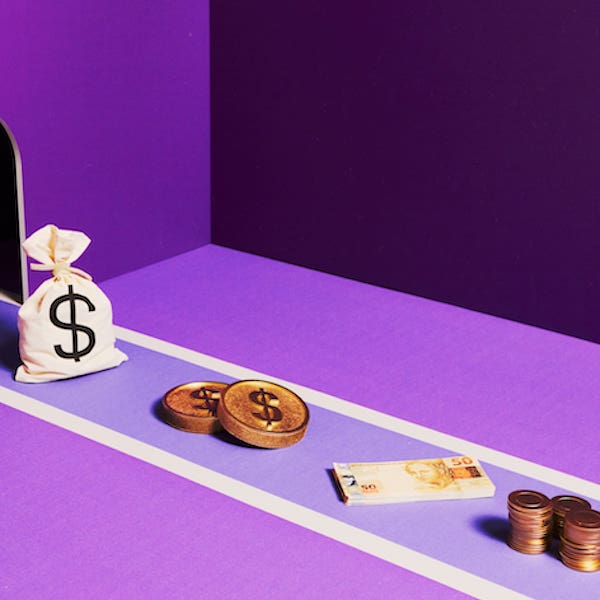 Imagem de uma sacolinha de dinheiro com um cifrão ($), duas moedas de cobre e um bolinho de dinheiro, em uma superfície roxa.