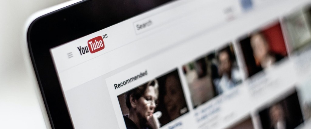 Tela de computador com o logo vermelho do YouTube no canto superior esquerdo e imagens desfocadas de vídeos da plataforma