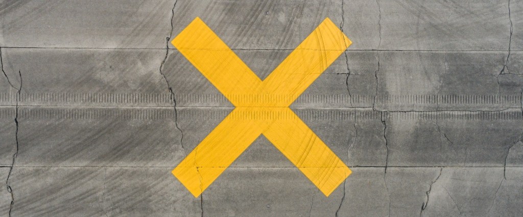 Golpe usando revisões do INSS: fotografia aérea de um X pintado em amarelo no asfalto. Créditos da imagem: Cole Ankneyv