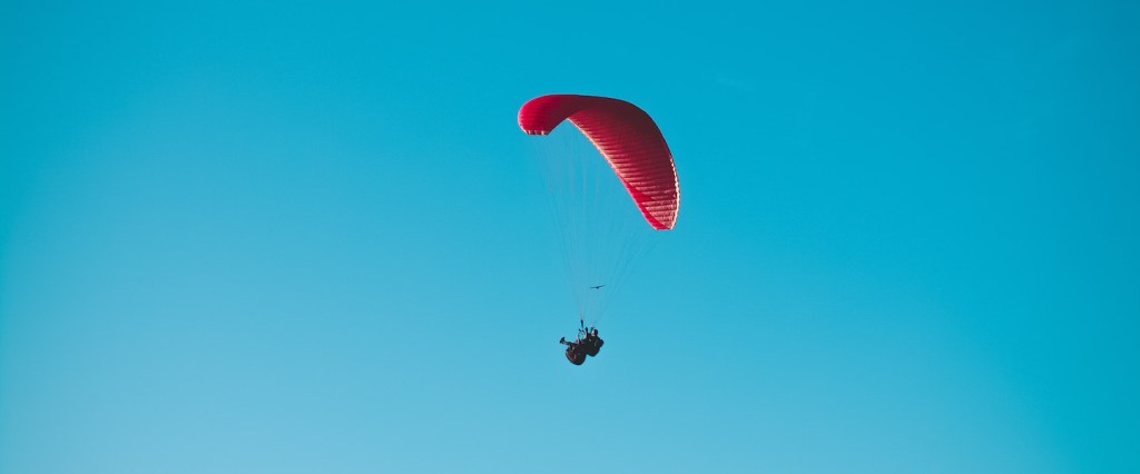 Nascidos em maio recebem quarta parcela do auxílio emergencial 2021: fotografia de uma pessoa com paraquedas vermelho num céu azul. Créditos da imagem: Alecsander Alvesv
