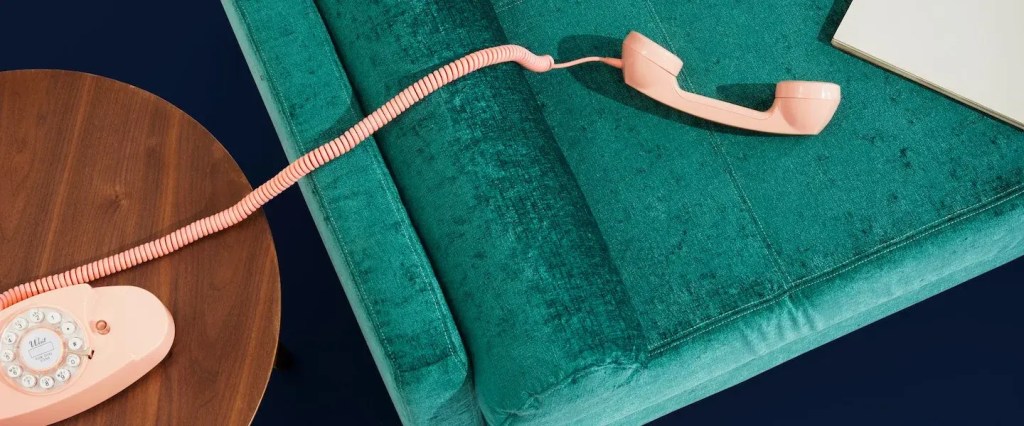 Foto vista de cima de um sofá verde com um telefone rosa fora do ganho e um caderno.