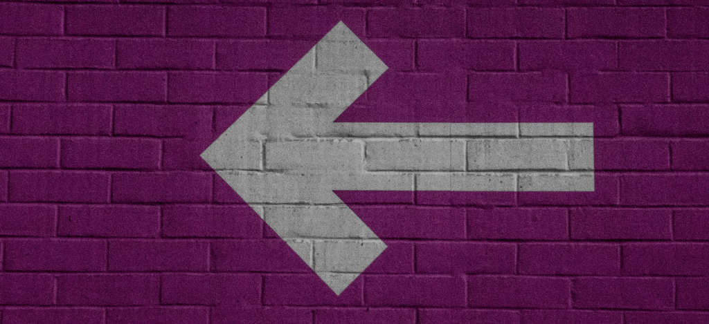 5 dúvidas comuns sobre cashback: Flecha branca, virada à esquerda, pintada em uma parede roxa. Créditos: Nick Fewings, Unsplash