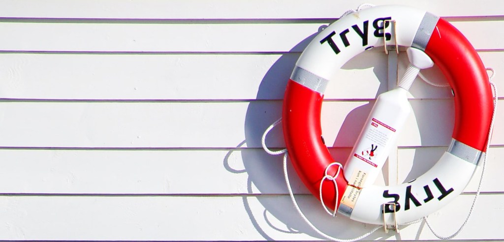 Foto de uma boia salva-vidas circular, presa na parede de um barco. A boia possui as cores vermelha e branca. O objetivo desta foto é ilustrar o conteúdo de resgate antecipado de seus investimentos.
