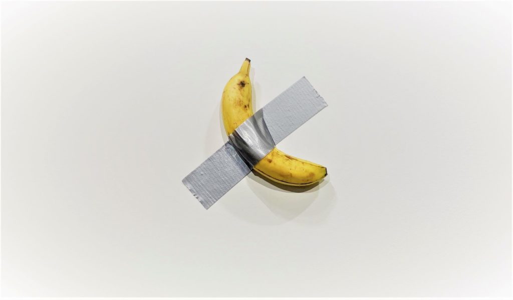 Em uma parede branca, uma banana está fixada com um pedaço de silver tape, uma fita adesiva prateada