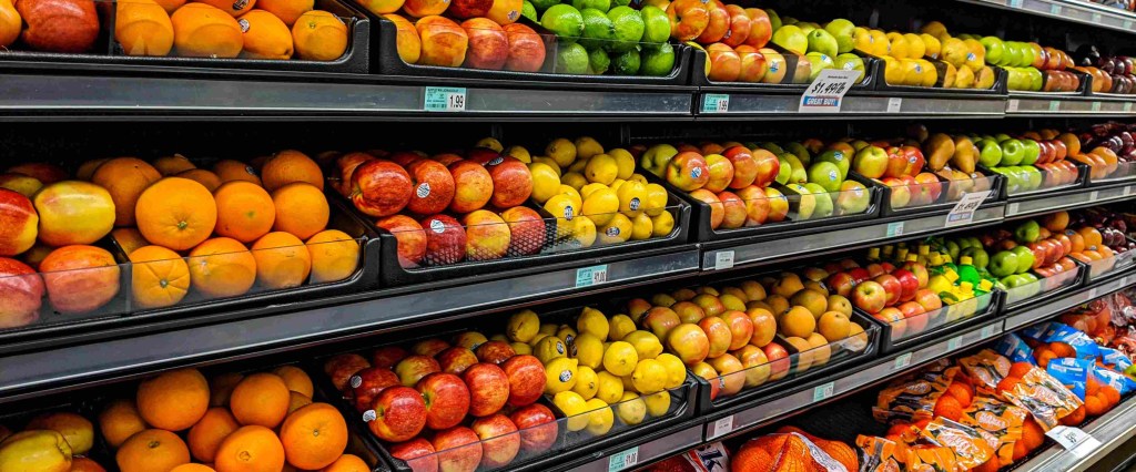 Prateleiras de um supermercado com frutas como maçãs e laranjas