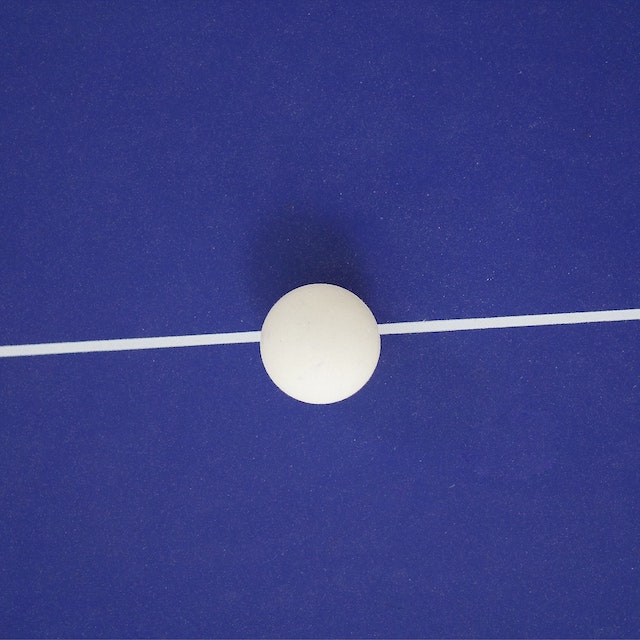 Stablecoin: fotografia de uma bolinha de ping pong branca sobre uma linha branca que cruza da direita pra esquerda no fundo azul. Créditos da imagem: Kiran Ck