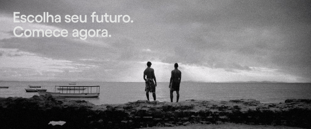 Campanha TV Nubank 2021: fotografia em preto e branco de dois homens em cima de pedras, à beira do mar, olhando para o sol se pondo ao fundo. No canto superior esquerdo da imagem, está escrito 