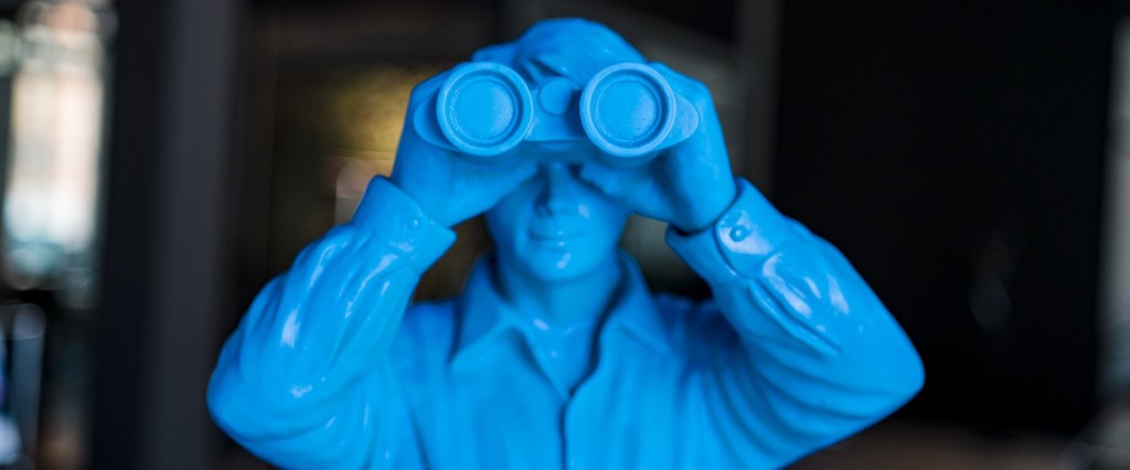 Como fica a poupança com a Selic acima de 8,5%: fotografia de um boneco miniatura azul olhando por um binóculos. Créditos da imagem: Julian Hochgesang