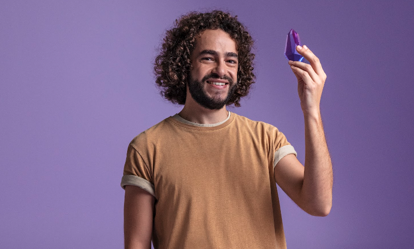 Um rapaz de camiseta bege segura um cristal roxo na mão.