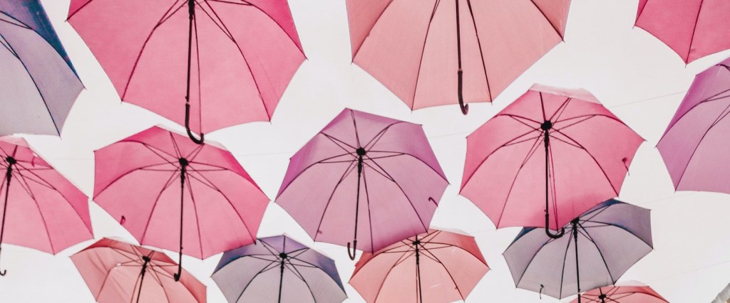 Imagem de vários guarda-chuvas em tons de rosa pendurados em um varal. Foto: Jonathan Borba/Unsplash