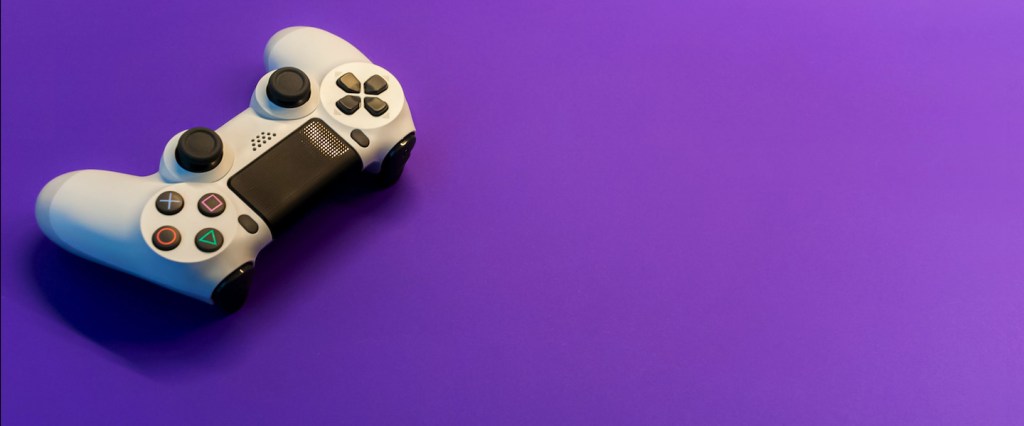 Nubank e Hype Games: parceria com descontos exclusivos. Um controle de videogame na cor cinza em fundo roxo. Créditos: Igor Karimov, unsplash.