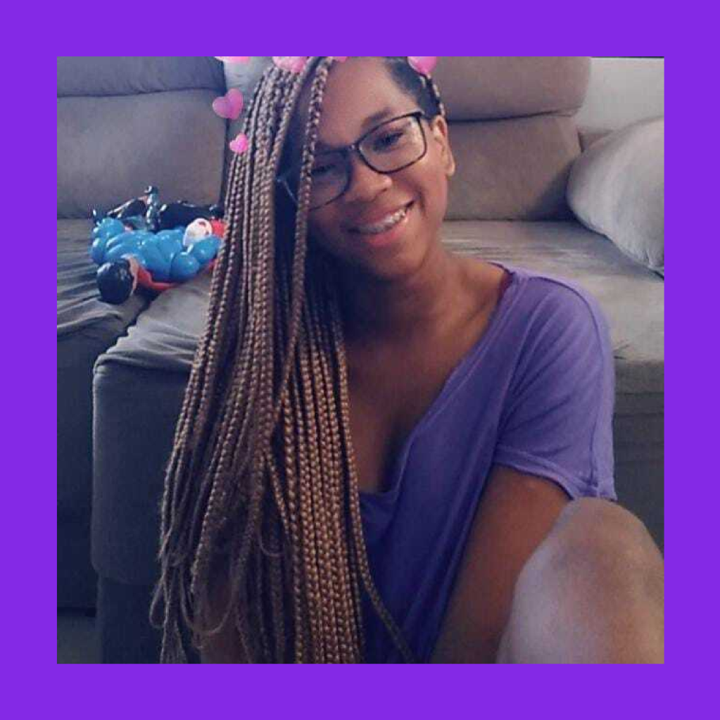 Imagem de Amanda, uma jovem negra, de tranças nos cabelos, com óculos, sorridente, e uma camiseta roxa