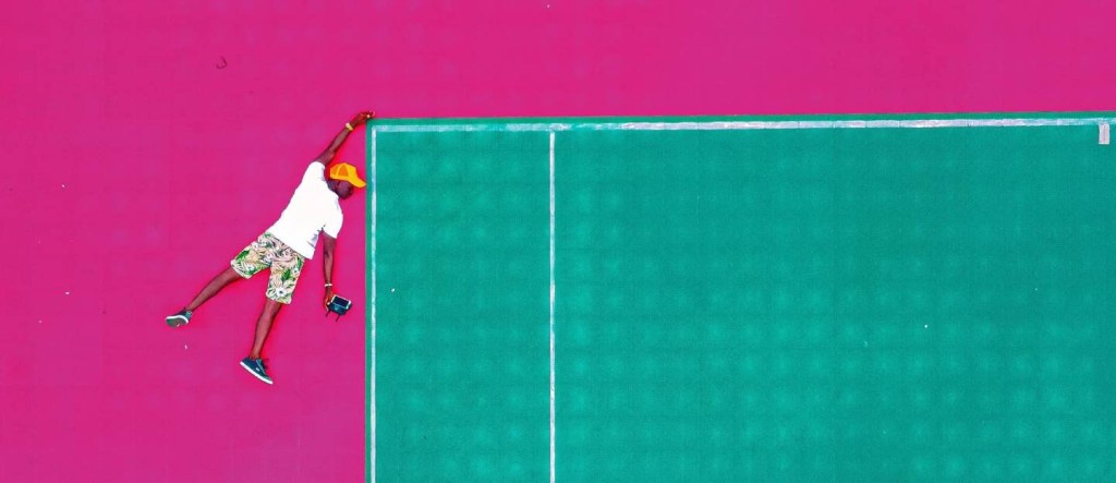 Compliance - Ilustração mostra foto de homem negro se pendurando em um bloco verde. O fundo da imagem é rosa.