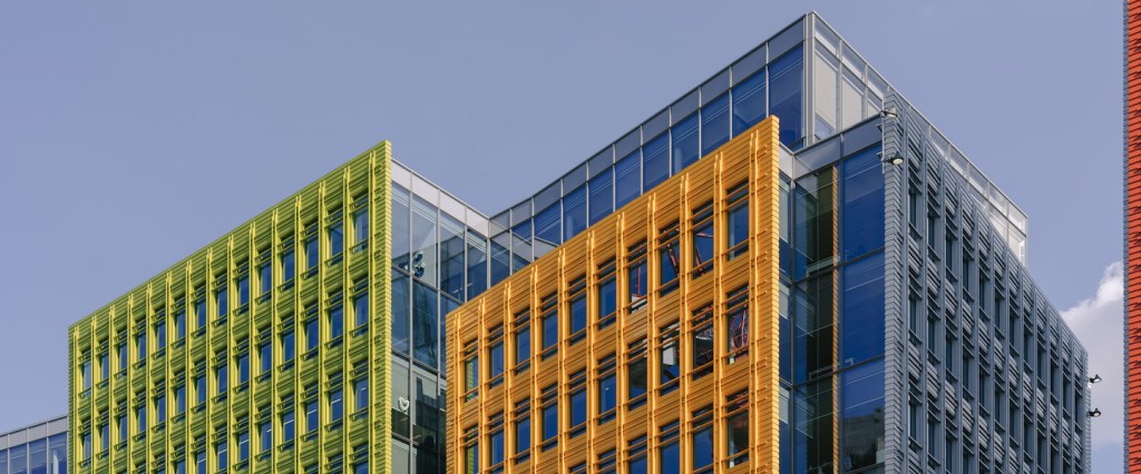 B2B: o que é esse modelo de negócio? Imagem de dois prédios lado a lado, com detalhes em verde e laranja, e céu ao fundo. Créditos: Luca Nicoletti, Unsplash.