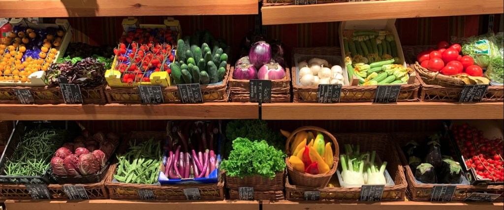 B2C: o que é esse modelo de negócio? Imagem de duas prateleiras de madeira em um supermercado cheio de verduras e legumes organizadas lado a lado. Créditos: Raúl González Escobar, Unsplash.