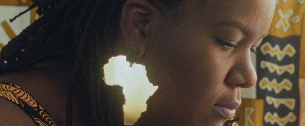 Toalá Antônia: imagem de Toalá, uma mulher negra, em postura pensativa com um brinco no formato do continente africano espelhado.