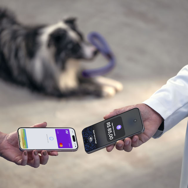 Imagem de uma mão feminina aproximando o celular com a tela no cartão Nubank para pagar por contactless, aproximando de outro celular, na mão de um veterinário. Tem um cachorro ao fundo. O cenário é um pet shop.