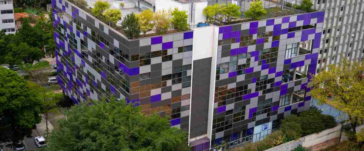 Na imagem aérea aparece o escritório do Nubank, um prédio cheio de janelas e com partes roxas, cercado de árvores