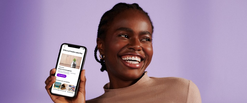 imagem mostra menina sorrindo com um celular na mão e a tela reflete a nova experiência de guardar dinheiro no app do Nu