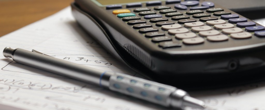 Imagem de uma calculadora e uma caneta apoiadas sobre um caderno com anotações