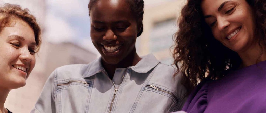 Nubank e Shopee: parceria com benefício exclusivo. Três mulheres sorrindo olhando para baixo a tela do celular.