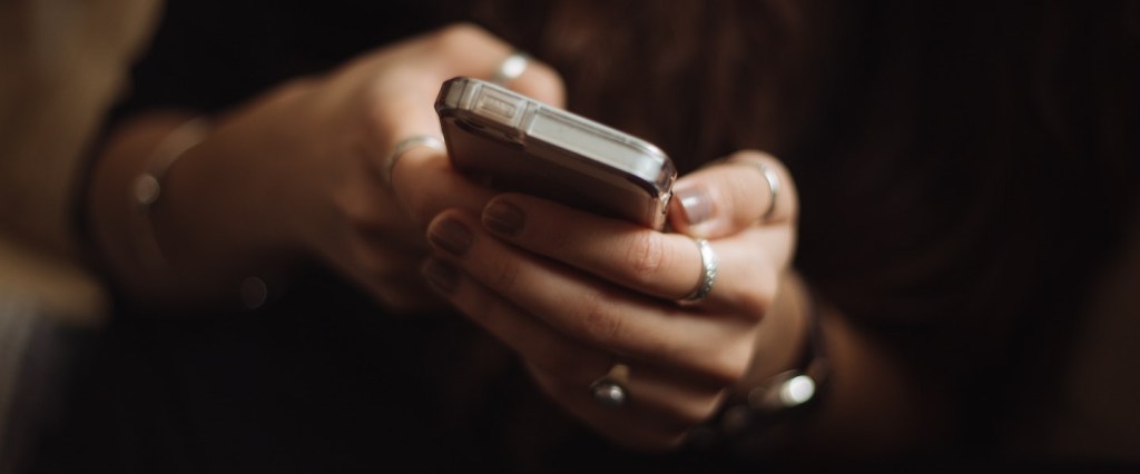 Golpe da portabilidade: imagem das mãos de uma mulher branca segurando um celular.