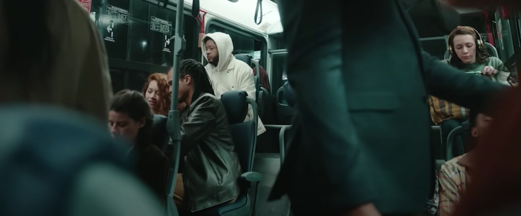Propaganda do Nubank: Imagem do cantor Emicida sentado em um ônibus com várias pessoas ao redor. Emicida veste um moletom branco com capuz.