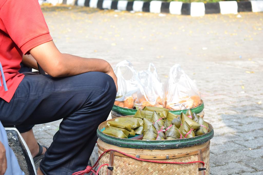 Mercado de trabalho - Imagem mostra um vendedor de frutas e pamonhas. Ele está sentado e veste uma calça azul e camisa vermelha.